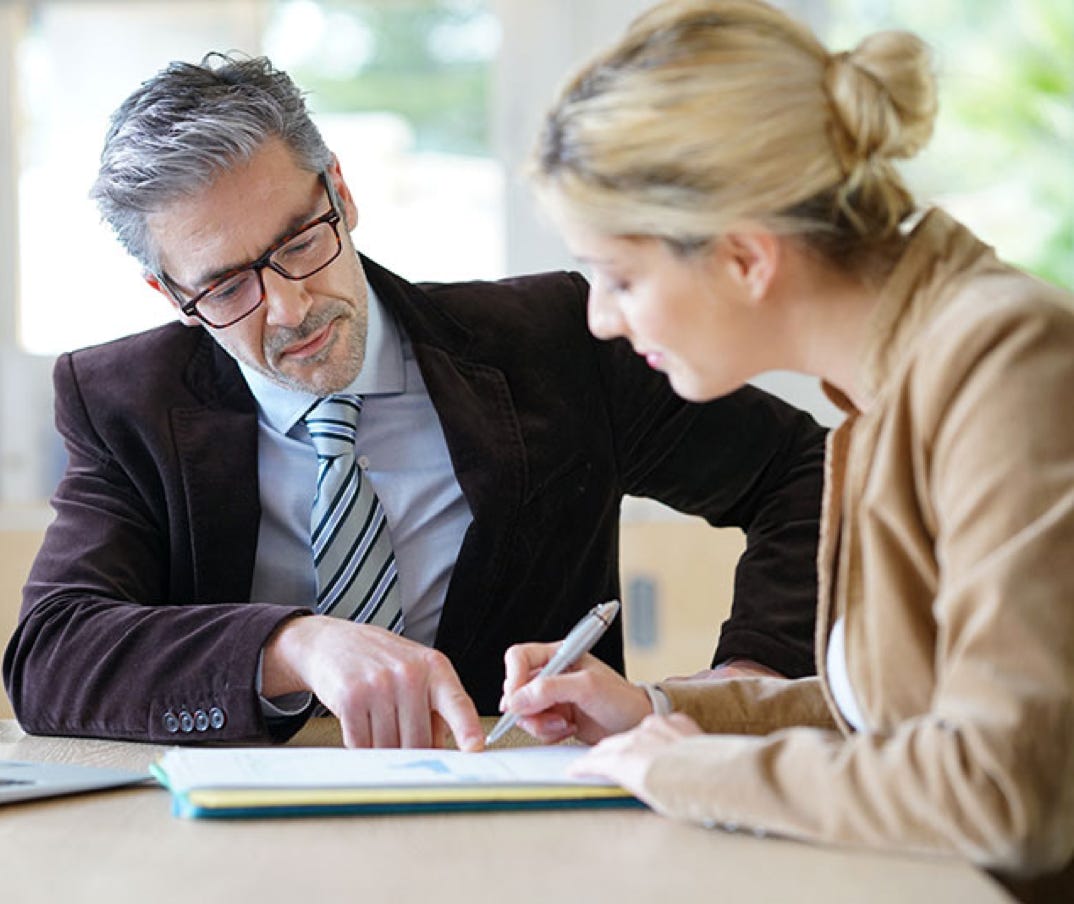 Ein Mann und eine Frau in Buisinesskleidung sitzen an einem Tisch und studieren ein vor ihnen liegendes Dokument